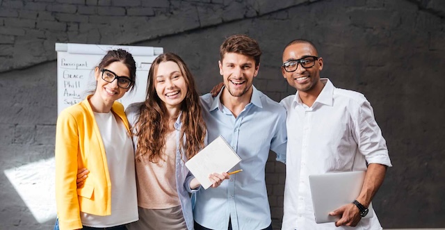 Gruppe von vier jungen Menschen schaut sichtlich erfreut zum Betrachter.