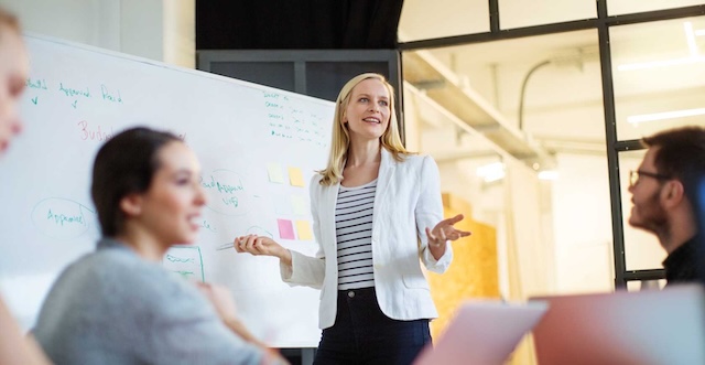 Dozentin in weißem Jacket präsentiert den Seminarteilnehmern die Tafelergebnisse.