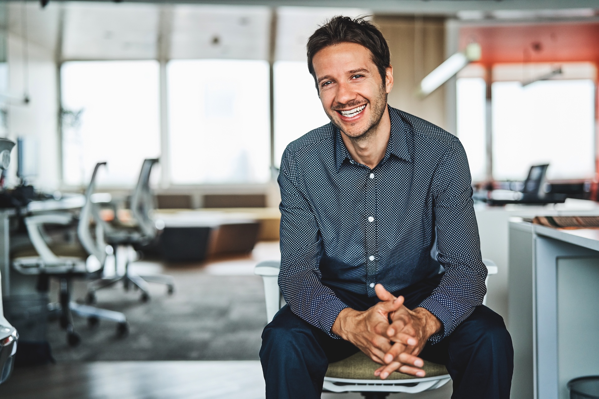 Ein Mann sitzt auf einem Stuhl am Schreibtisch und ist seitlich zum Betrachter gedreht.